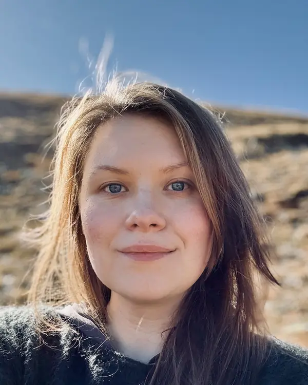 Anna Melnyk outdoors on a sunlit hillside, blue sky behind her.